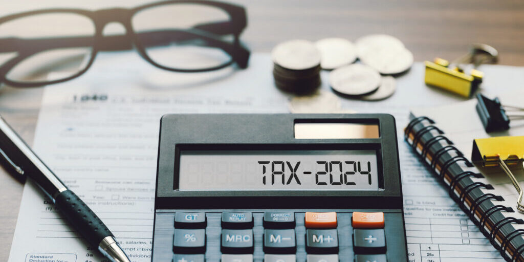 Word Tax 2024 on the calculator. Business and tax concept.Calculator, coins, book, tax form, and pen on table.Tax deduction planning.Financial research, government taxes, and calculation tax return